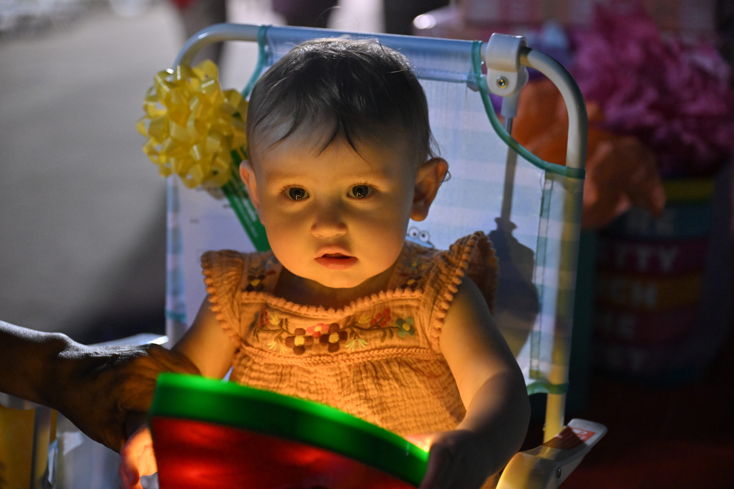 A baby in a striped chair, lit by a single light pool at a first-birthday party