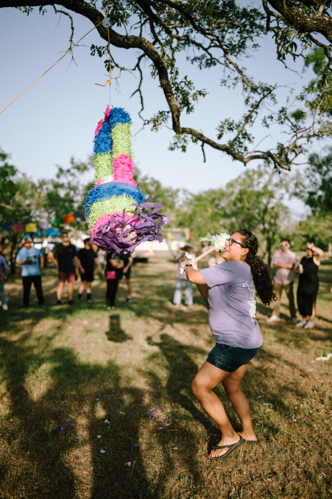 A guest swinging at a tall colorful piñata hanging from an oak tree at golden hour