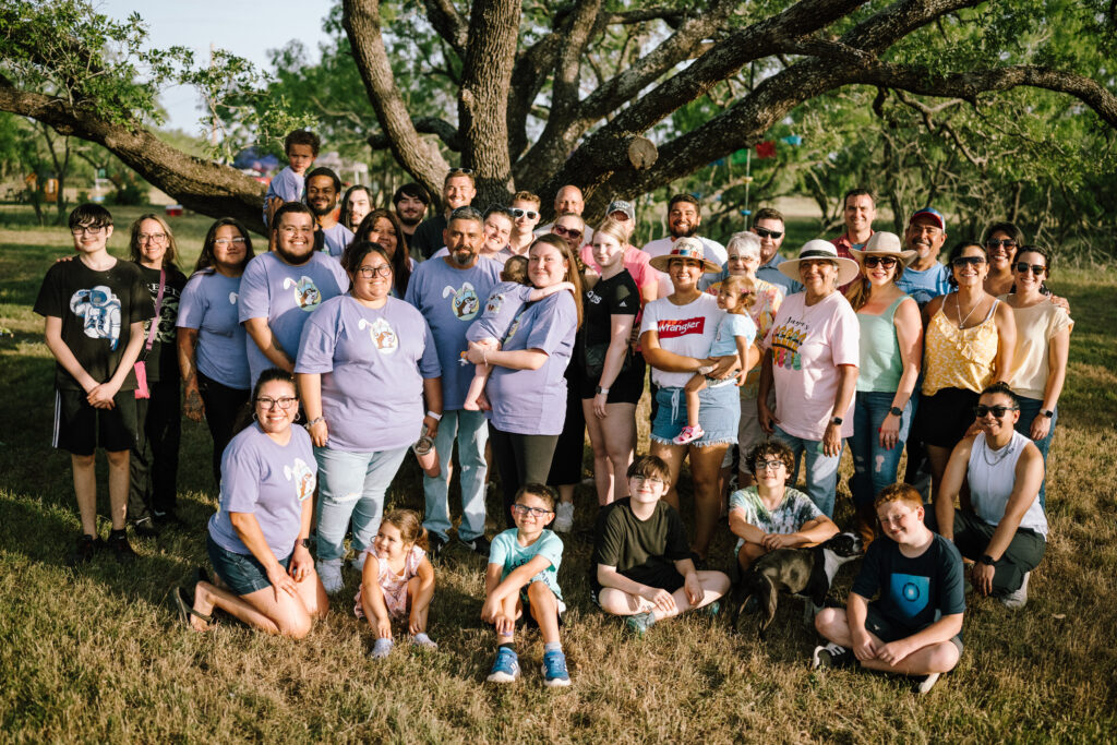 An extended family group portrait under a sprawling oak tree, matching lavender shirts