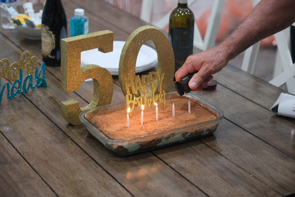 Glittering '50' decoration and candles being lit on a tiramisu cake at a fiftieth birthday